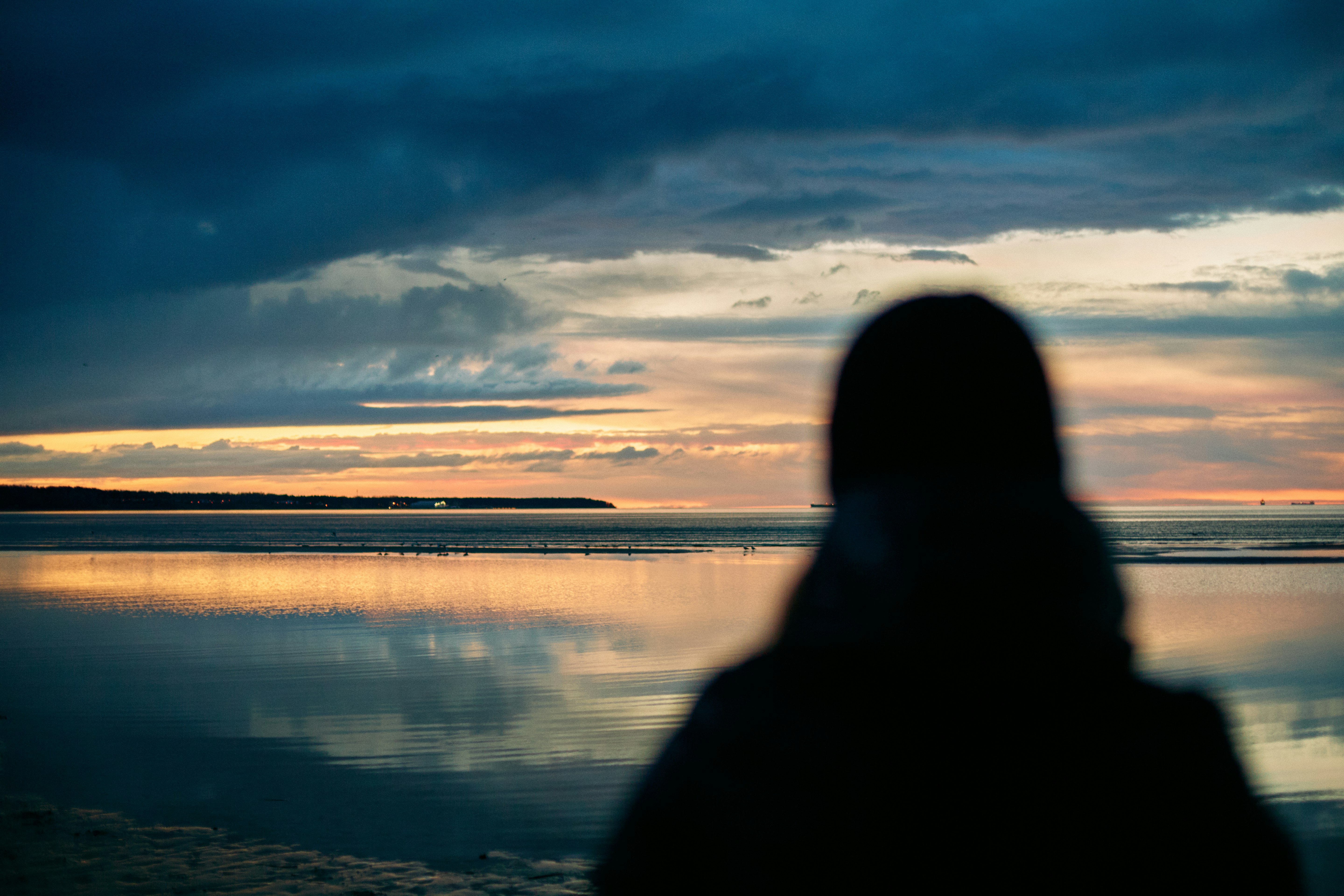 silhouette of person standing near body of water during sunset